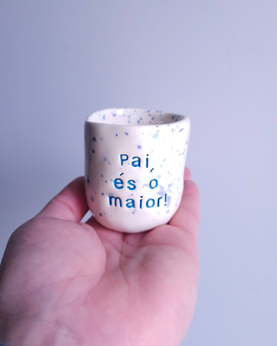 Copo de café pequeno em cerâmica artesanal com salpicado azul e a frase "Pai, és o maior!" gravada, modelo Inês da Tia Cila.