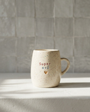 Caneca em cerâmica creme com salpicado multicolor e frase gravada Super avô em vermelho e azul com coração dourado, Tia Cila