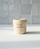 Copo de café em cerâmica creme com salpicado colorido e frase gravada Caga nisso, Tia Cila