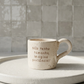 caneca de ceramica artesanal com pega salpicada em bege colocada sobre um prato branco com a frase nao tenho tamanho imagina paciencia marca tia cila