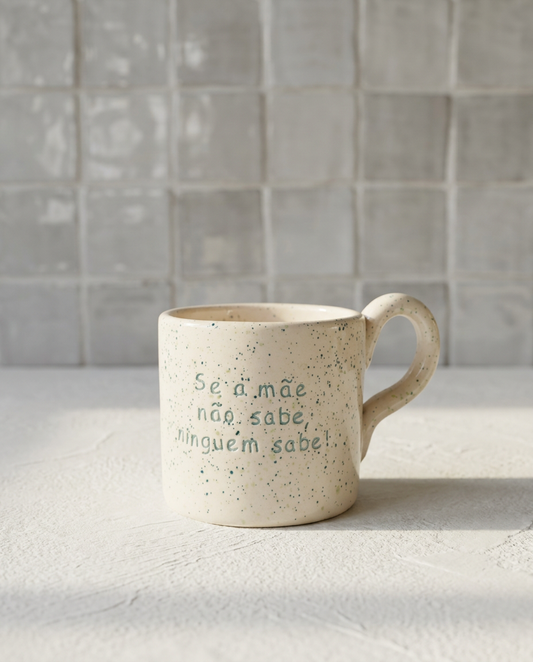 Caneca de cerâmica artesanal com asa (Modelo Francisca) de cor creme com salpicos verdes, personalizada com a frase "Se a mãe não sabe, ninguém sabe!" gravada em verde.