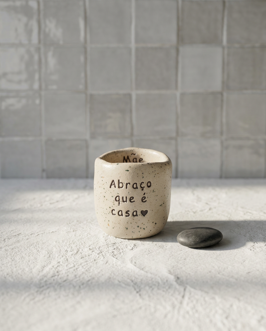 Copo de café artesanal sem asa (Modelo Inês) em cerâmica salpicada, com a frase gravada "Abraço que é casa" seguido de um coração, e a palavra "Mãe" no interior.