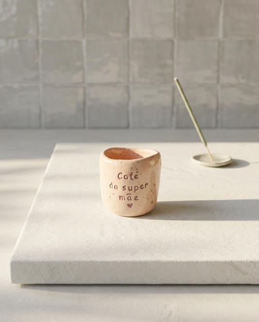 Copo de café artesanal sem asa (Modelo Inês) em cerâmica com salpicos coloridos e a frase "Café da super mãe" gravada com um pequeno coração, ao lado de um incenso aceso.