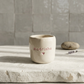 Copo de cerâmica artesanal modelo Inês, em tom creme com salpicados rosa pastel. No centro, a palavra "Madrinha" e um coração gravados em baixo relevo com cor rosa, sob luz solar natural.
