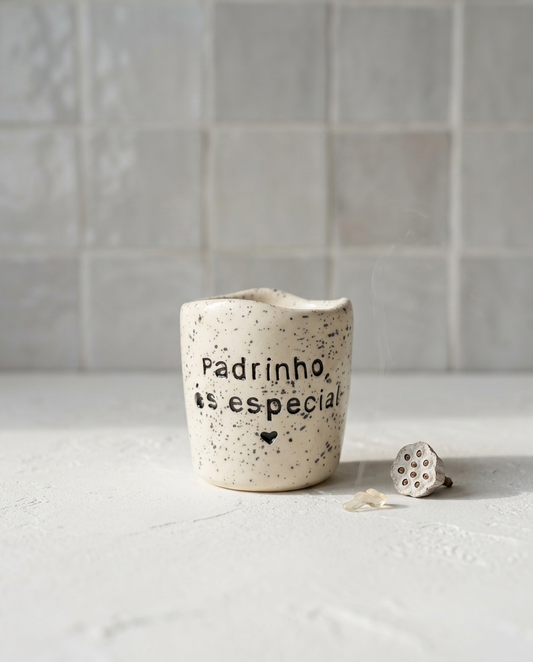 Copo de cerâmica artesanal modelo Inês, cor creme com salpicados esuros. Ao centro, a frase "Padrinho, és especial" gravada em baixo relevo com um pequeno coração, fotografado com luz natural.
