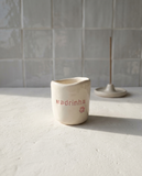 Copo de cerâmica artesanal modelo Inês, cor creme, decorado com flores em relevo pintadas em tons de rosa ao redor da palavra "Madrinha".