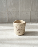 Copo de cerâmica artesanal modelo Inês, cor creme com salpicados escuros. Apresenta a frase "Gosto muito de ti" gravada no exterior e a palavra "Padrinho" no rebordo interior, sobre uma base de pedra.
