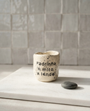 Copo de cerâmica artesanal modelo Inês, cor creme com salpicados escuros. Apresenta a frase "Padrinho, o mito, a lenda!" gravada no exterior, fotografado sobre uma placa de mármore.